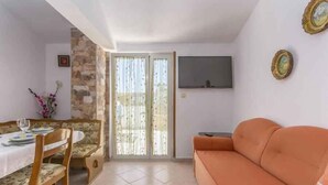 A living room with a sofa, a dining table with chairs, a TV mounted on the wall, and a sliding glass door leading to an outdoor area. - Holiday apartment with Wi-Fi and balcony (Dajla)