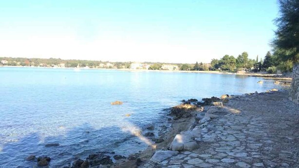 A coastal area with a stone pathway leading to the water, a clear sky, and distant buildings. - Holiday apartment with Wi-Fi and balcony (Dajla)