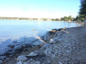 A coastal area with a stone pathway leading to the water, a clear sky, and distant buildings. - Holiday apartment with Wi-Fi and balcony (Dajla)