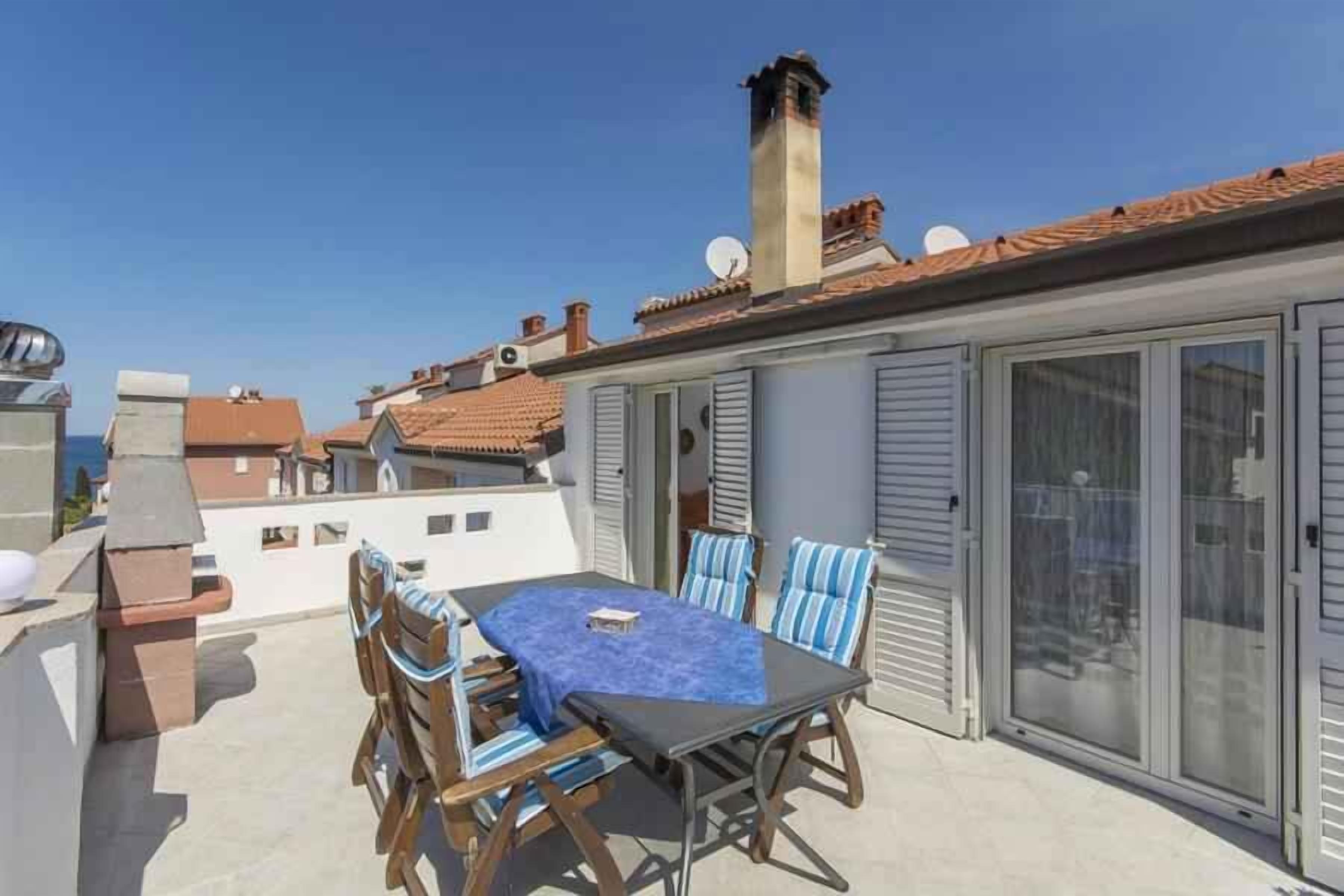 A rooftop terrace with a table and chairs, a chimney, and a sliding glass door.