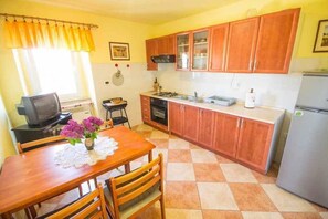 A compact kitchen with wooden cabinets, a dining table with chairs, a refrigerator, and a television. - Holiday Apartment Lovely Apartment Bencic with Balcony and Sea View (Novigrad)