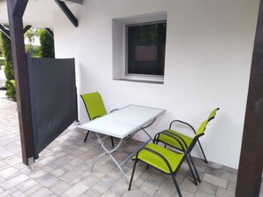 En uteplats med ett vitt bord och två gröna stolar, ett fönster och en delvis utsikt över en byggnads fasad.