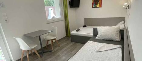A modern hotel room with a bed, a desk, a chair, a TV, and a window.