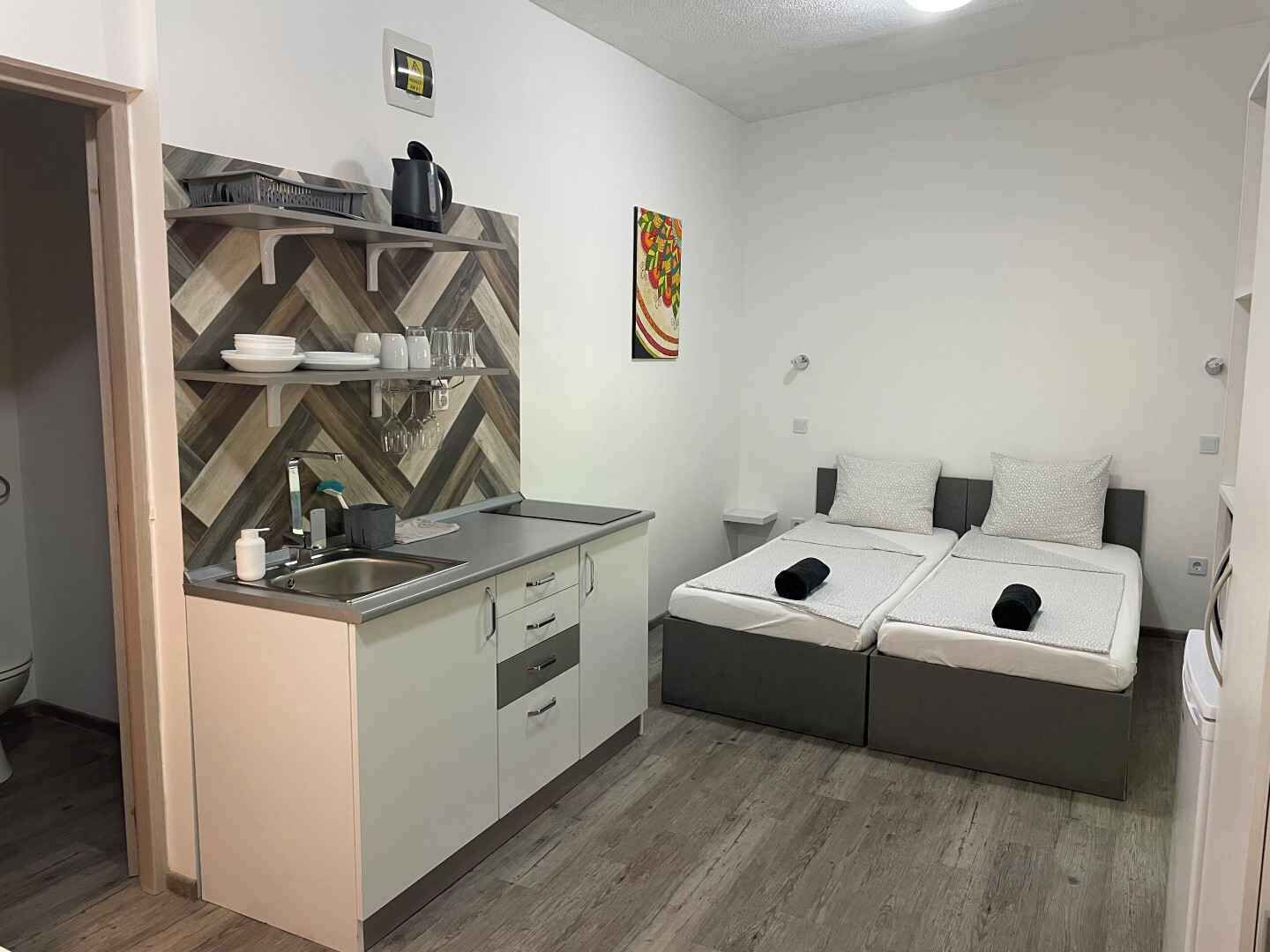 Une petite cuisine équipée d’un évier, d’une cuisinière et d’un four à micro-ondes. On y trouve un lit avec deux oreillers et une petite table de chevet.