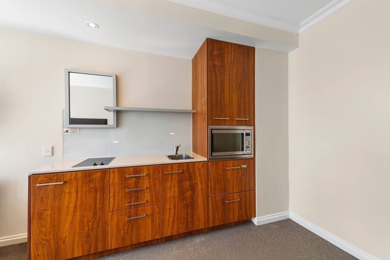 A kitchenette with a microwave, a sink, and wooden cabinetry.