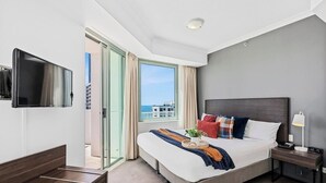 Ein Hotelzimmer mit Bett, Fernseher, Nachttisch, Lampe und einem Fenster mit Vorhängen.