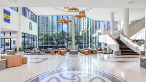 Eine geräumige Lobby mit einer zentralen Sitzecke, einer Treppe und großen Fenstern mit Blick auf die umliegenden Gebäude.