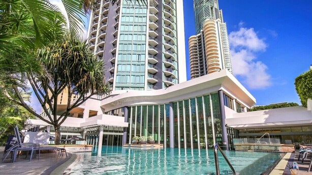 Ein Hotel mit Schwimmbad, Palmen und hohen Gebäuden im Hintergrund.