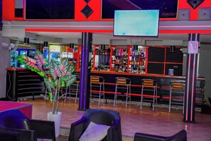 A bar area with seating, a television screen, and a variety of bottles on shelves.