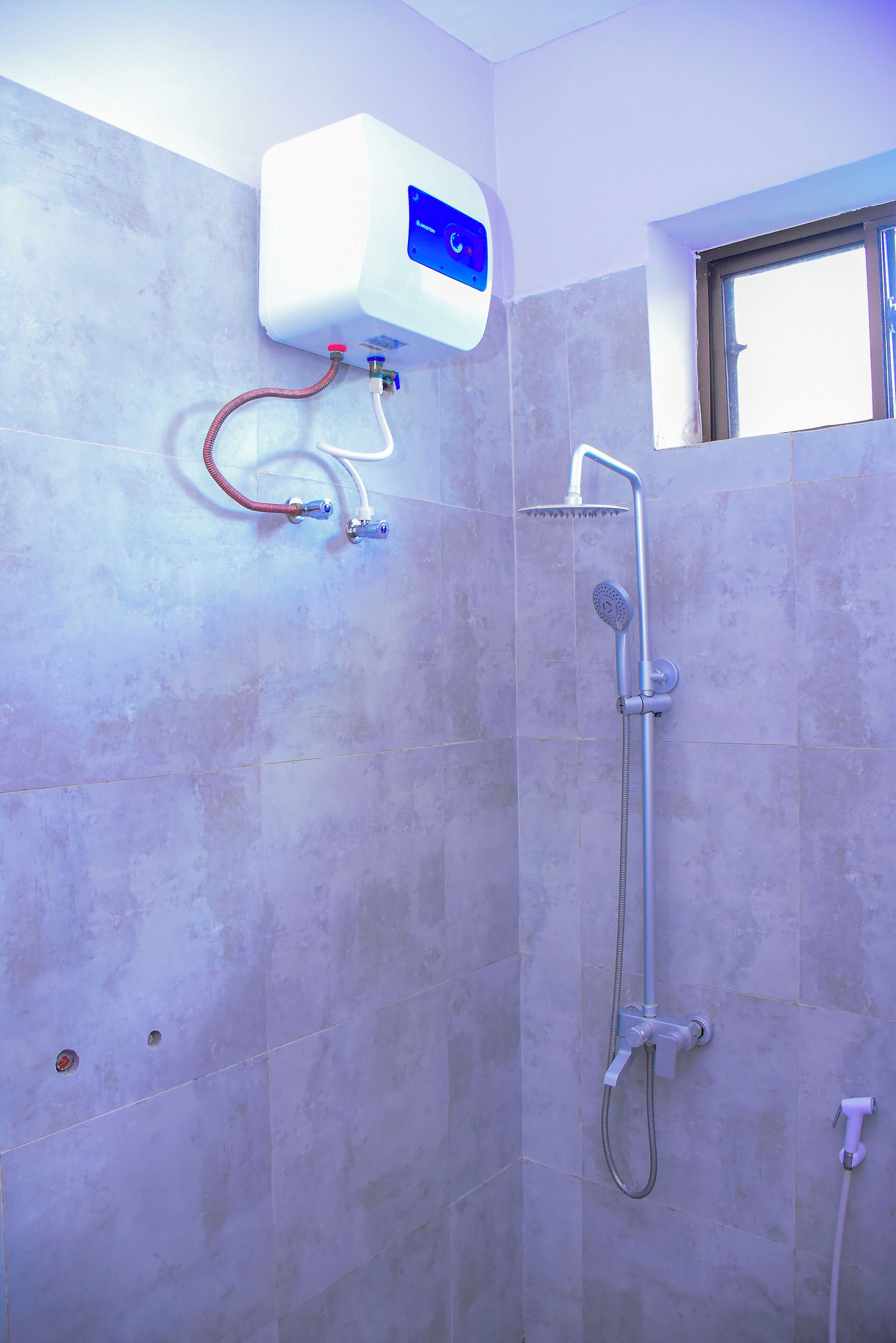 A bathroom with a shower, a water heater, and a window.