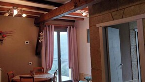 Una habitació amb sostre de fusta, una taula amb cadires, una finestra amb cortines i una porta.