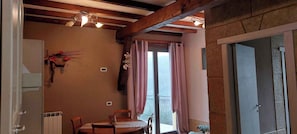 Ein Zimmer mit Holzbalkendecke, einem Tisch mit Stühlen, einem Fenster mit Vorhängen und einer Tür.