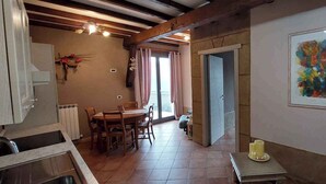 Zona de menjador amb taula i cadires, espai de cuina amb armaris, una porta que condueix a una altra habitació i un quadre abstracte emmarcat a la paret.