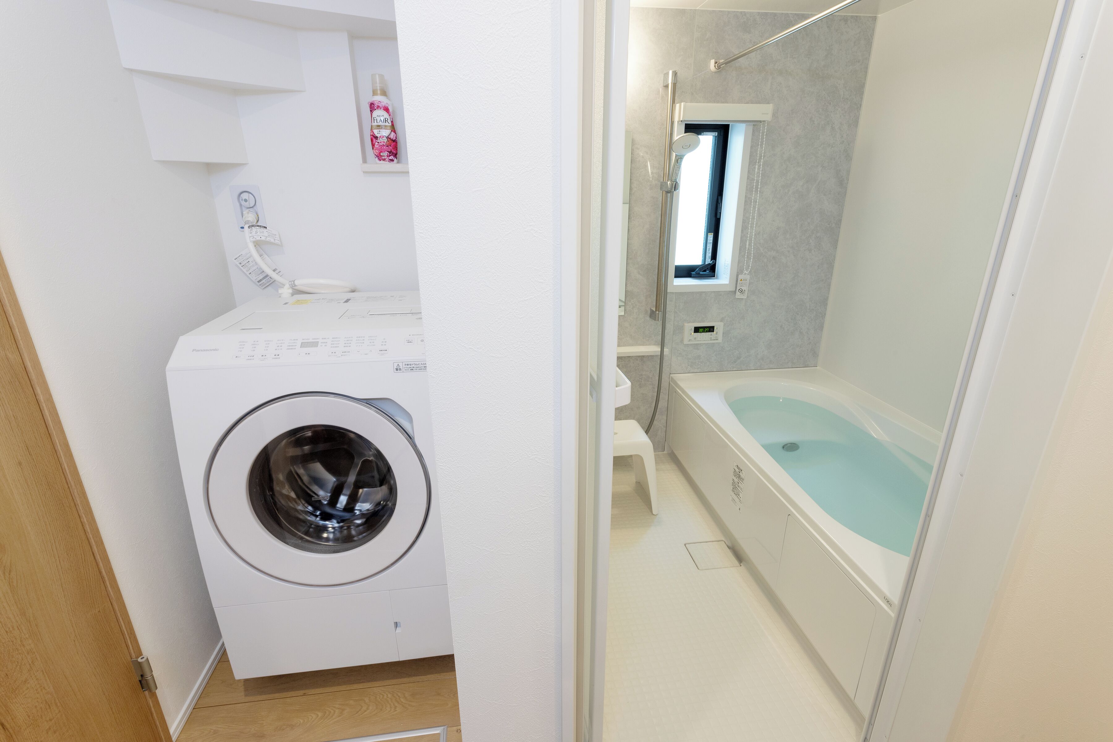 A compact bathroom with a washing machine, a bathtub, and a small window.