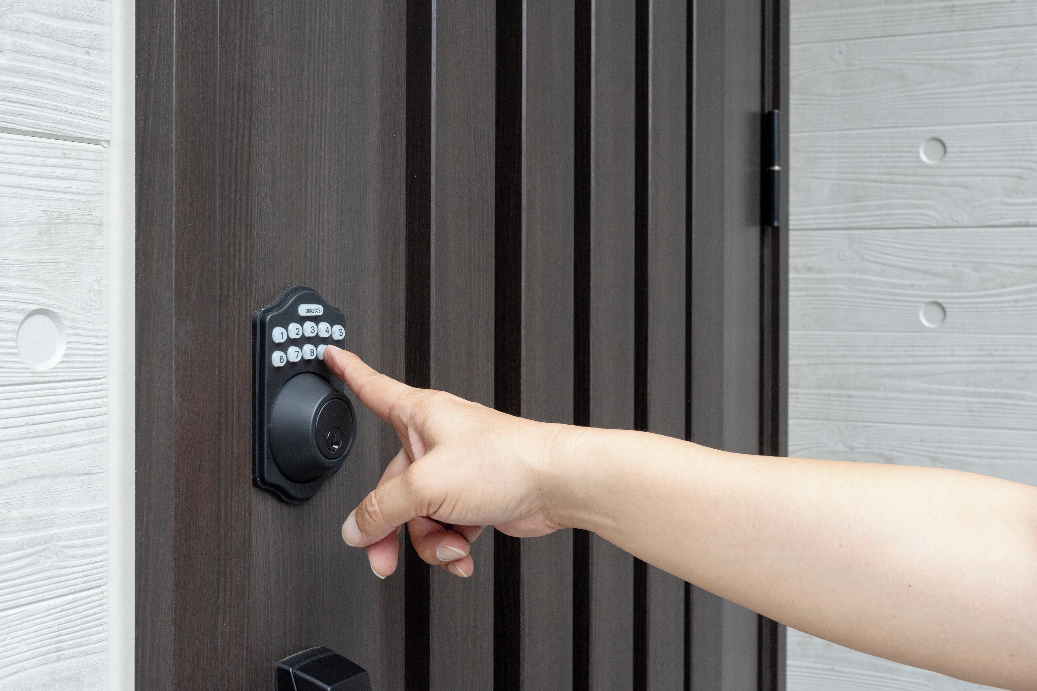 A hand pressing a keypad on a door lock.