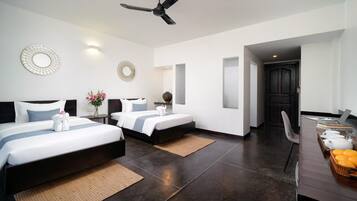 A hotel room with two beds, a ceiling fan, a desk with a laptop, and a door leading to another room.