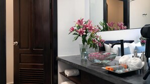 Une salle de bain avec une porte en bois foncé, un miroir, un lavabo, un bol en verre contenant des fleurs roses, une serviette et des articles de toilette.