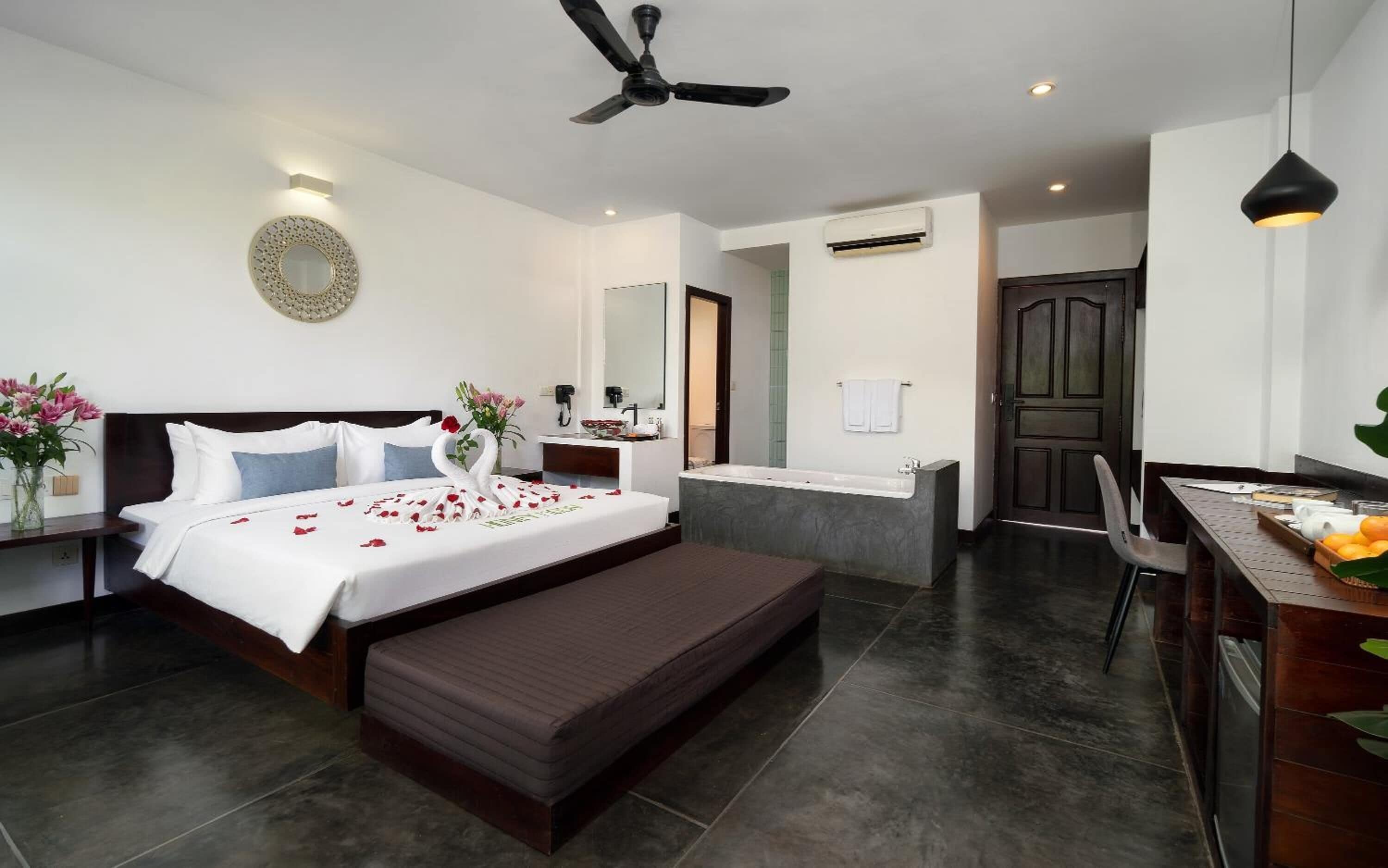 A modern hotel room with a bed, bedside table, vanity, and a desk with a chair.