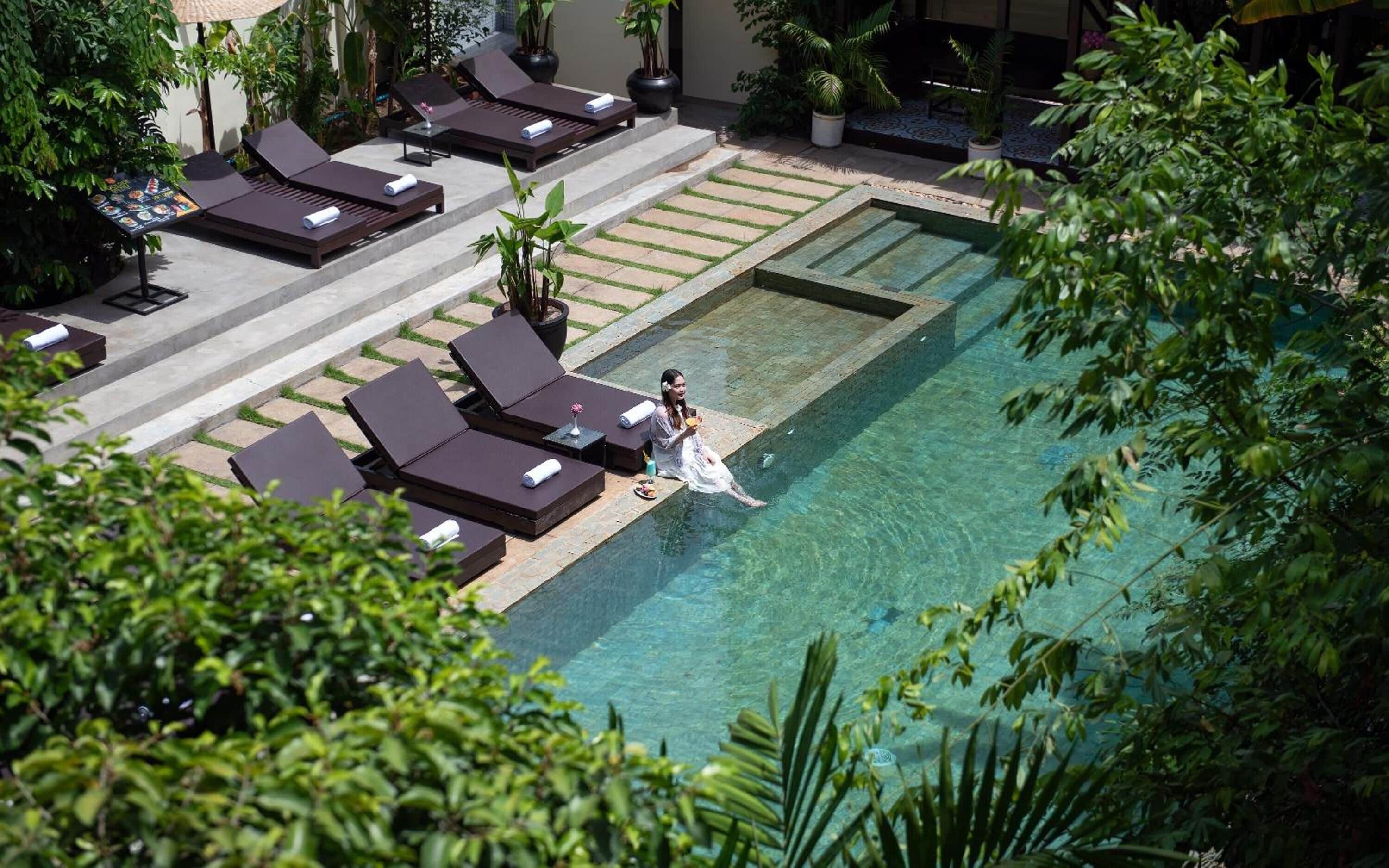 A poolside area with lounge chairs and a woman sitting by the pool.