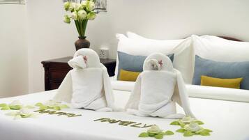 A hotel room with a bed, two towels with red flowers, a vase with white flowers, and a 'Happy Family' decoration on the bed.