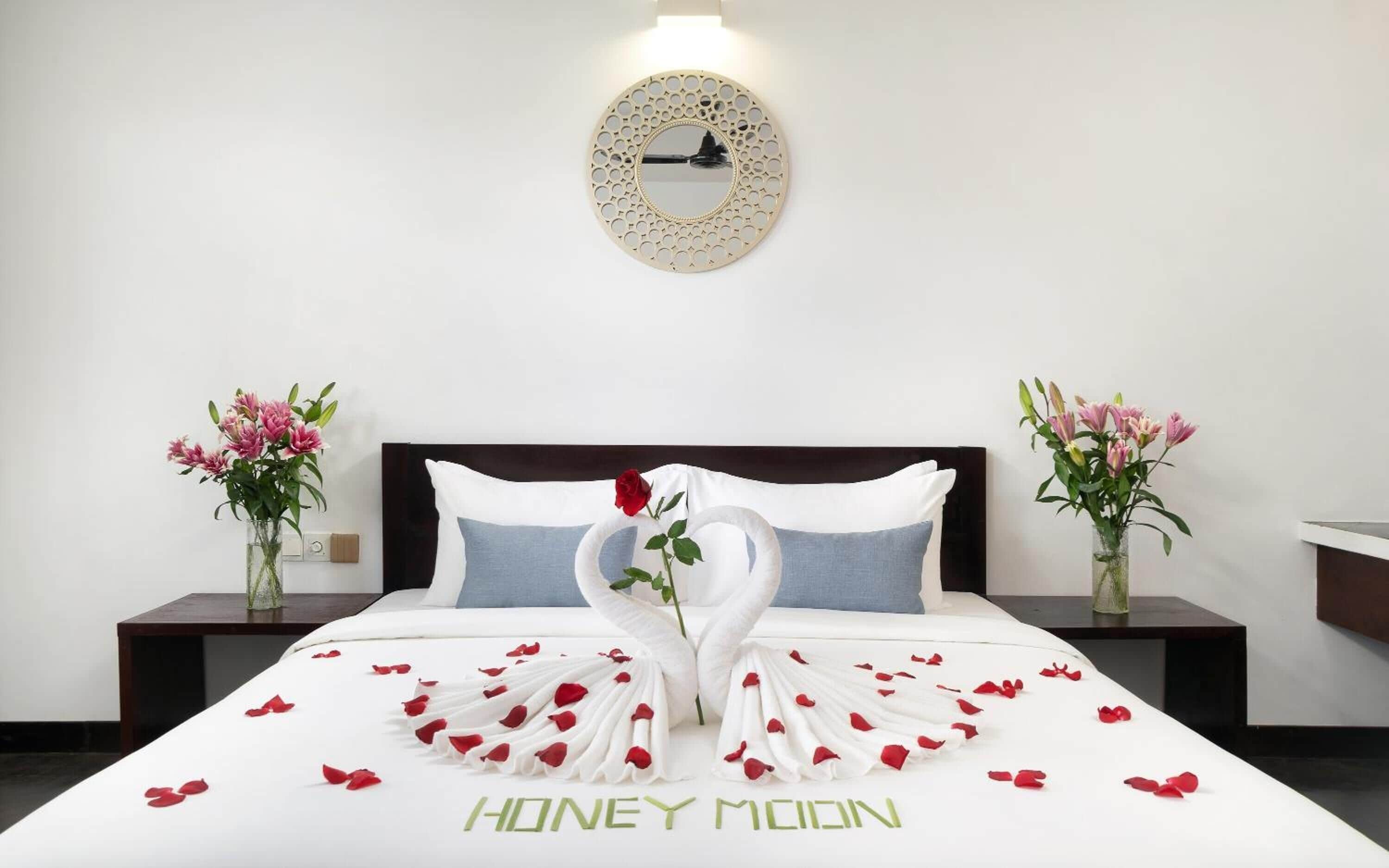 A hotel room with a bed, a round mirror, and two vases with flowers.