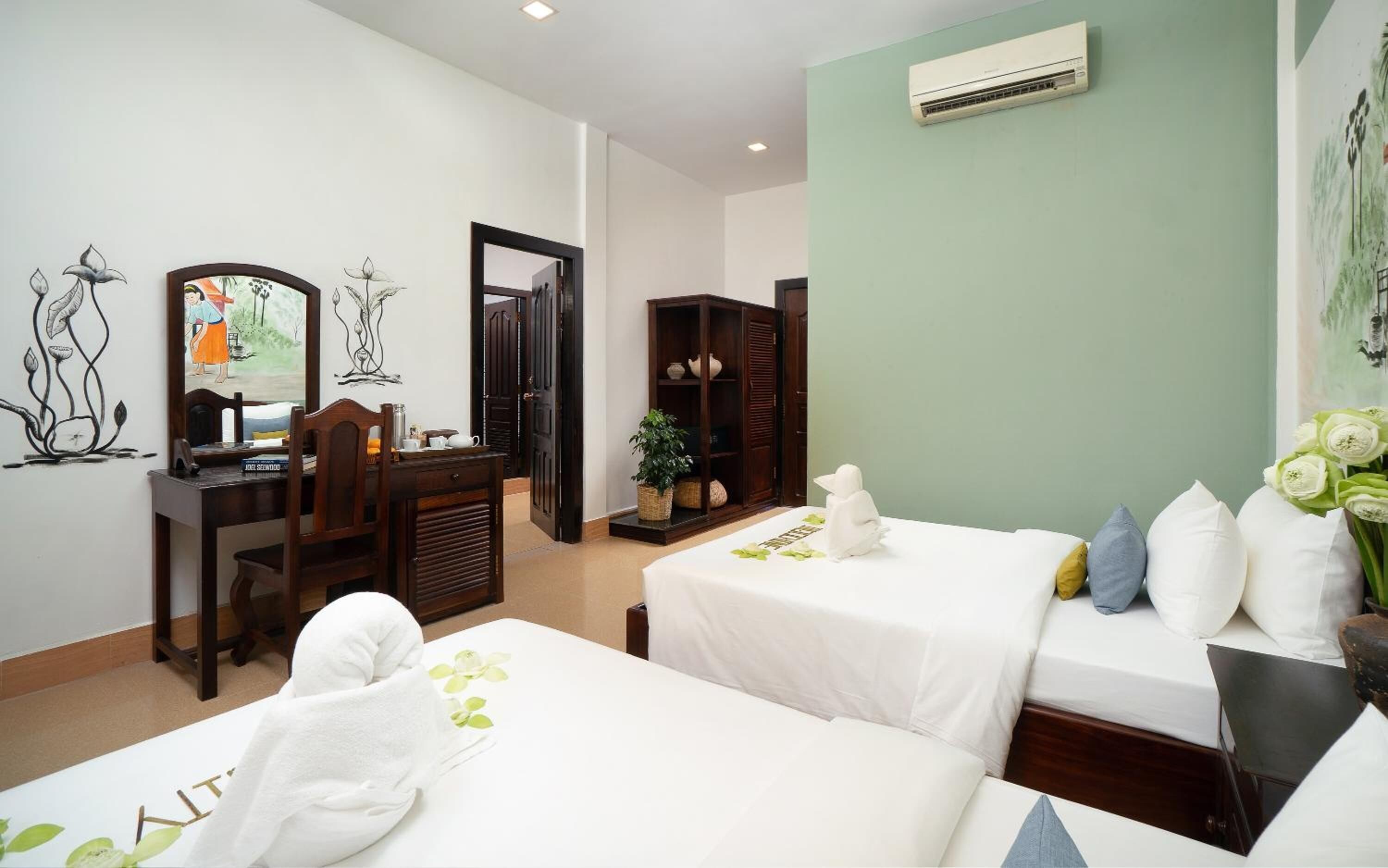 A hotel room with two beds, a desk, a chair, a wardrobe, and an air conditioning unit.