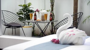 Une chambre d’hôtel avec un lit, une table à manger avec des chaises, un vase avec des fleurs et des bouteilles de bière.