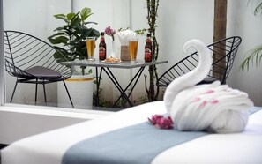 Habitación de hotel con una cama, una mesa de comedor con sillas, un florero con flores y botellas de cerveza.