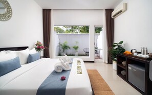 Habitación de hotel con cama, cartel de bienvenida, pequeño balcón con plantas y kitchenette.