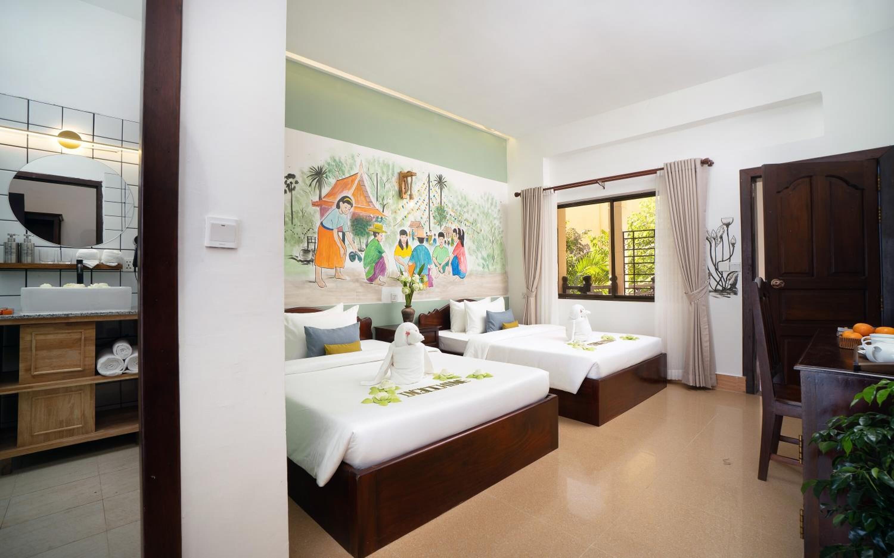 Una habitación de hotel con dos camas, baño, zona de comedor y un mural en la pared.