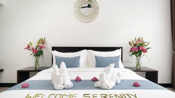Una cama bien hecha con toallas, un letrero de bienvenida y dos jarrones con flores.
