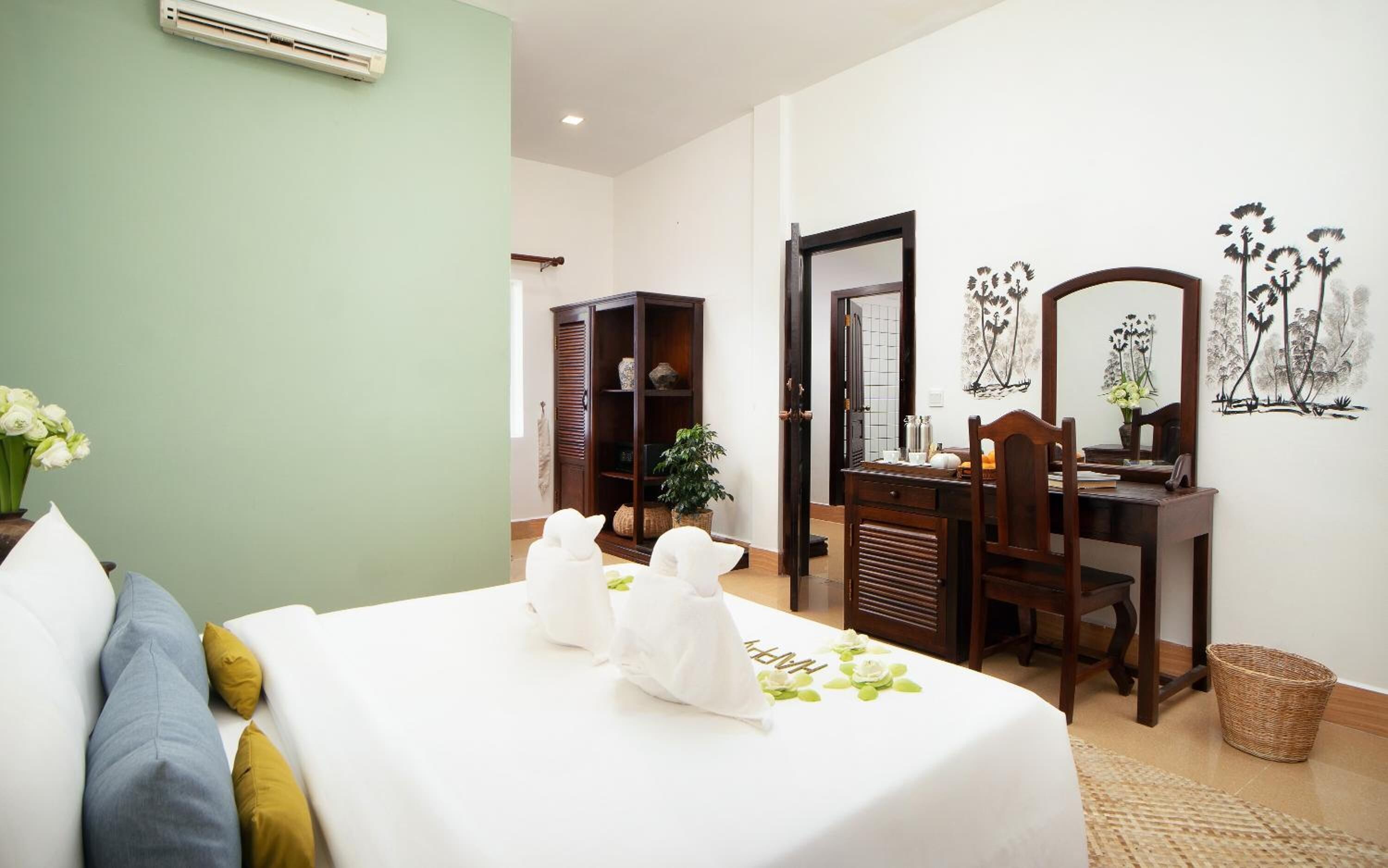 Habitación de hotel con cama, escritorio, silla, espejo y una pared decorada con obras de arte.