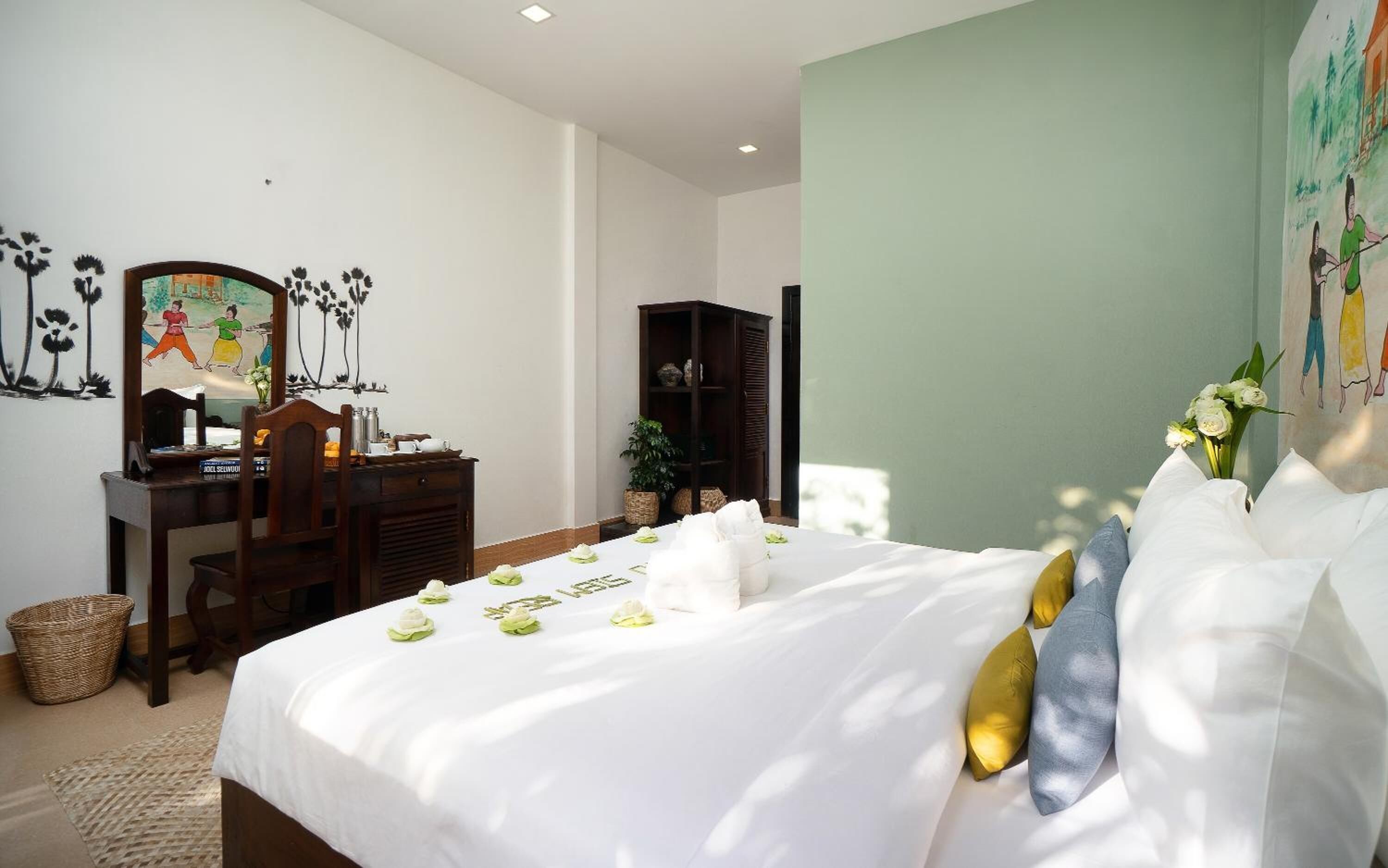 A hotel room with a bed, a desk, a chair, a bookshelf, and a painting on the wall.