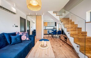 Ein modernes Wohnzimmer mit einer Couch, einem Esstisch mit Kerzen, einer Treppe mit Holzhufen und einer Küche im Hintergrund.