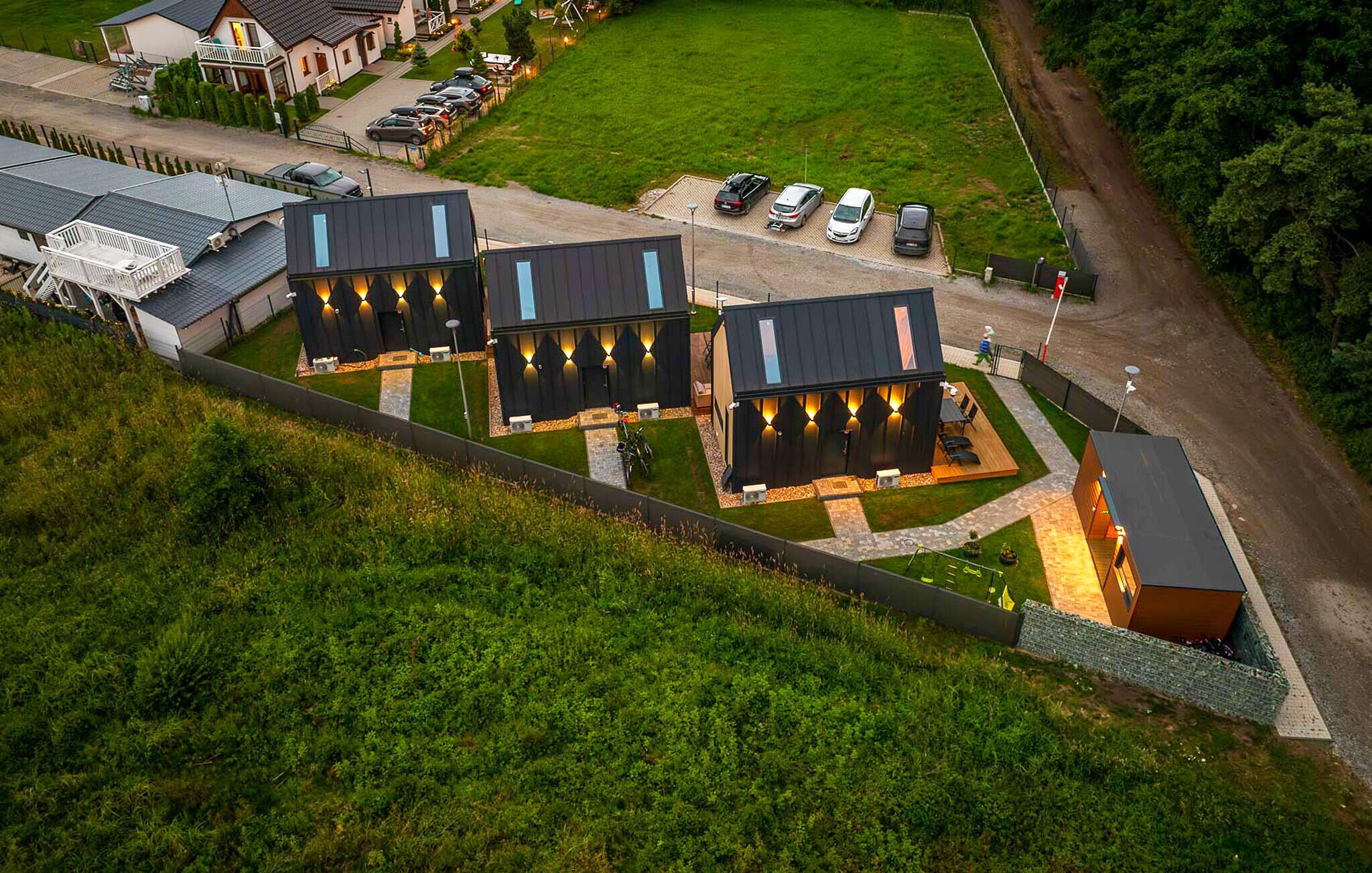 A modern building with multiple rooms, a parking area, and a grassy field.