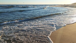 Uma praia com ondas, um cais e céu claro.