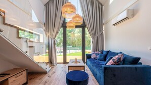 Uma sala de estar moderna com um sofá azul escuro, um banquinho preto redondo e uma mesa de vidro.