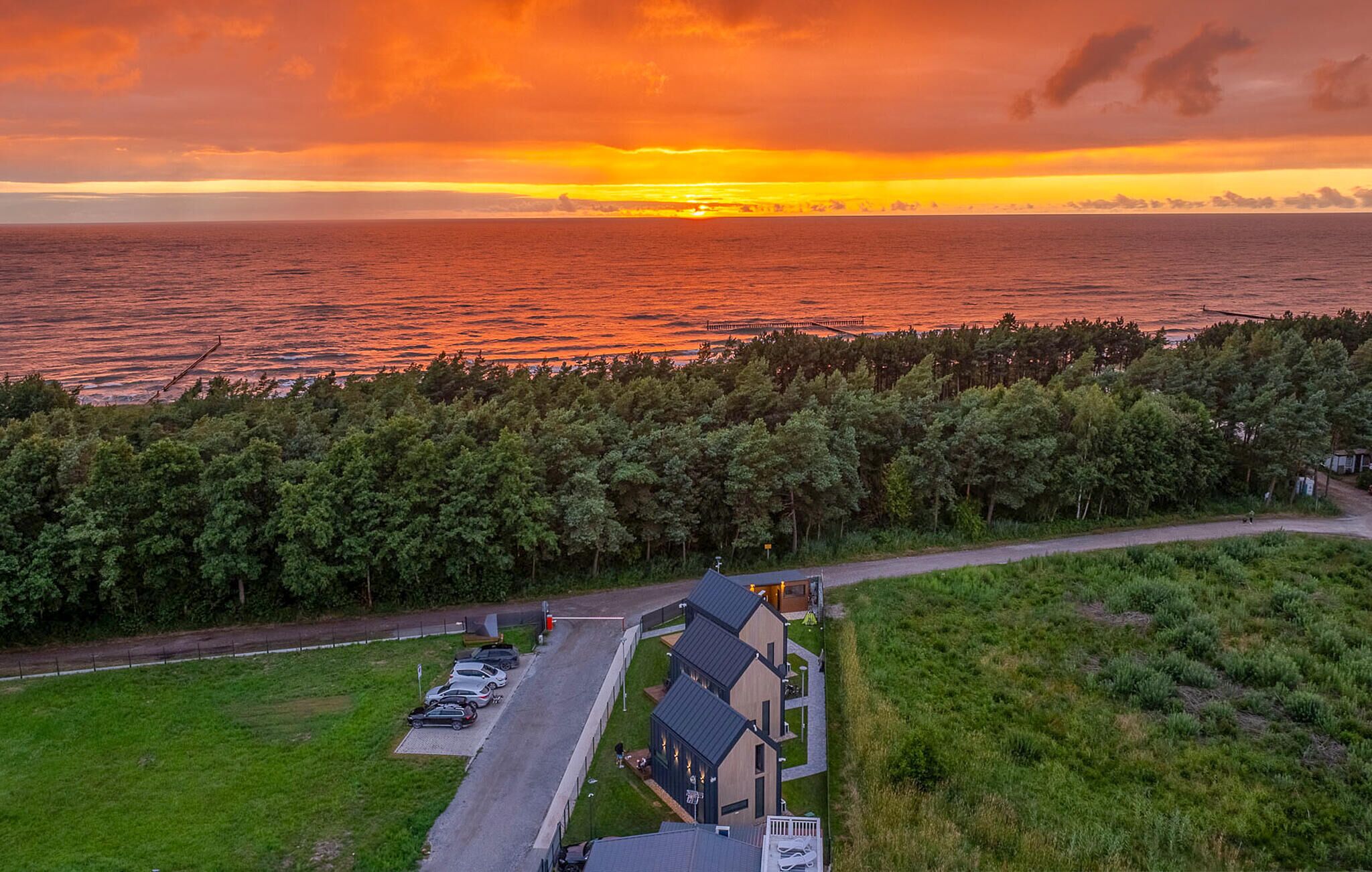 Um imóvel costeiro com área de estacionamento, um edifício com telhado inclinado e vista para o mar ao pôr do sol.