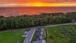 Um imóvel costeiro com área de estacionamento, um edifício com telhado inclinado e vista para o mar ao pôr do sol.