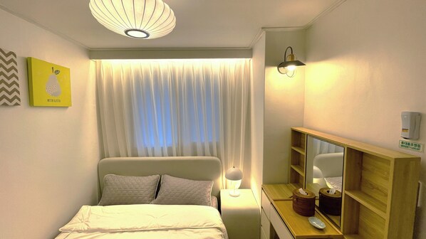 Ein Hotelzimmer mit einem Bett, einem Nachttisch mit Lampe, einem Spiegel, einem wandmontierten Luftreiniger und einem Fenster mit durchsichtigen Vorhängen.