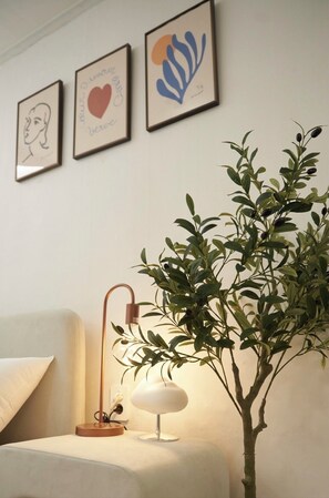 Ein Zimmer mit einem Bett, einer Nachttischlampe, einem an der Wand befestigten Bilderrahmen und einer Topfpflanze.