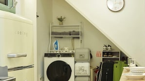 A compact kitchen with a washing machine, a small table, and a green suitcase.
