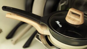 A kitchen with a black pan on a stove, a wooden handle, and a glass lid with the brand 'Menio' visible.