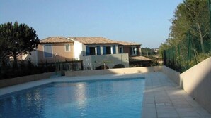 Une piscine avec une terrasse carrelée, un bâtiment doté d’un toit en tuiles et une clôture.