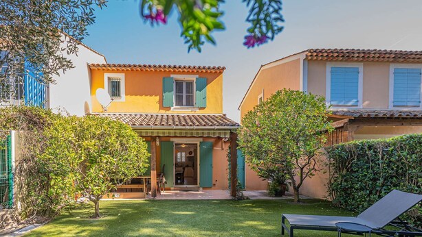 Une maison à deux étages, avec un toit en tuiles, un petit porche à l’avant et une pelouse bien entretenue.
