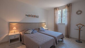 Une chambre avec deux lits, une table de chevet, une fenêtre avec des rideaux, un tableau accroché au mur et une lampe sur pied.