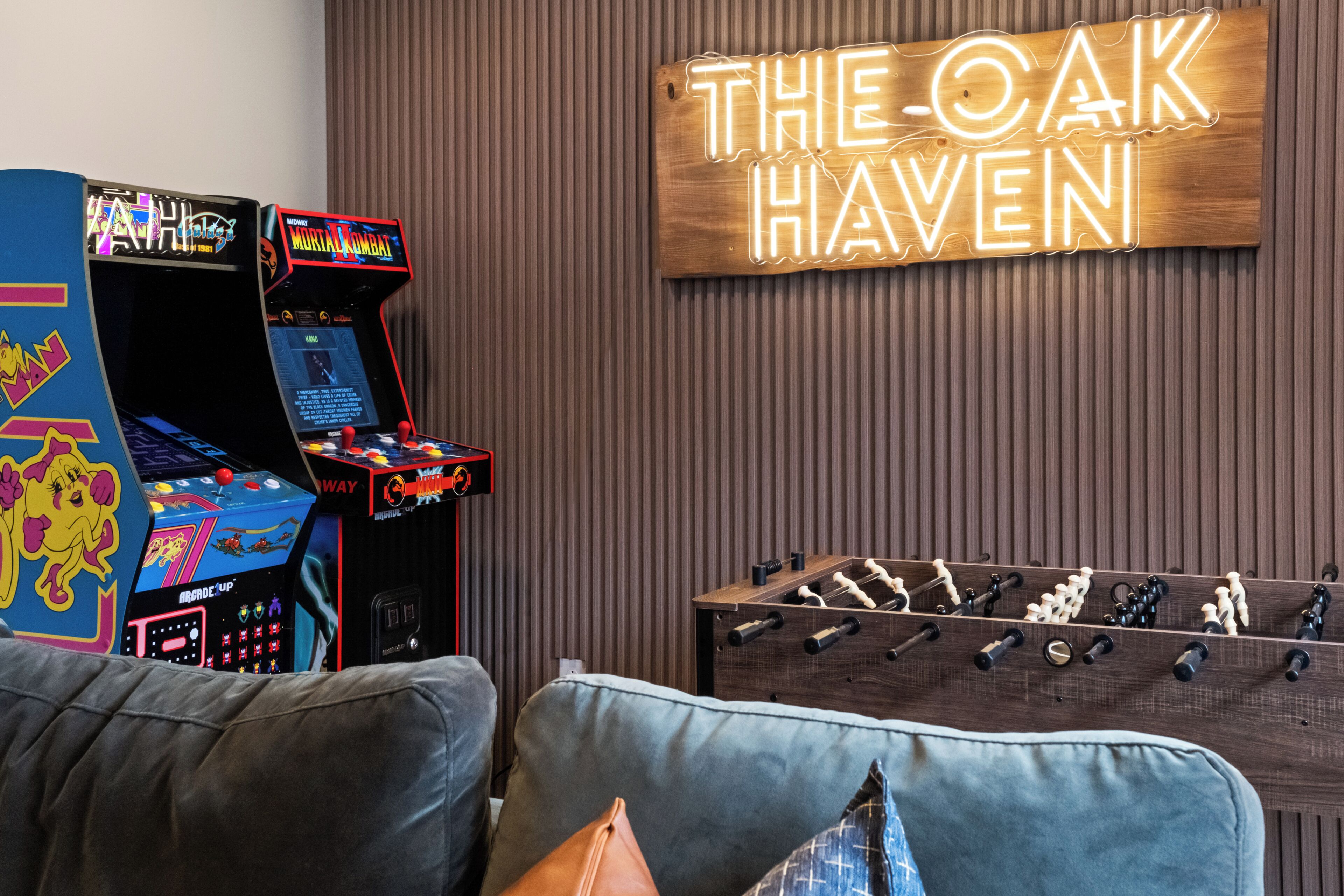 Ein Zimmer mit einem Kicker, zwei Spielautomaten und einem Neon-Schild mit der Aufschrift 'THE OAK HAVEN'.