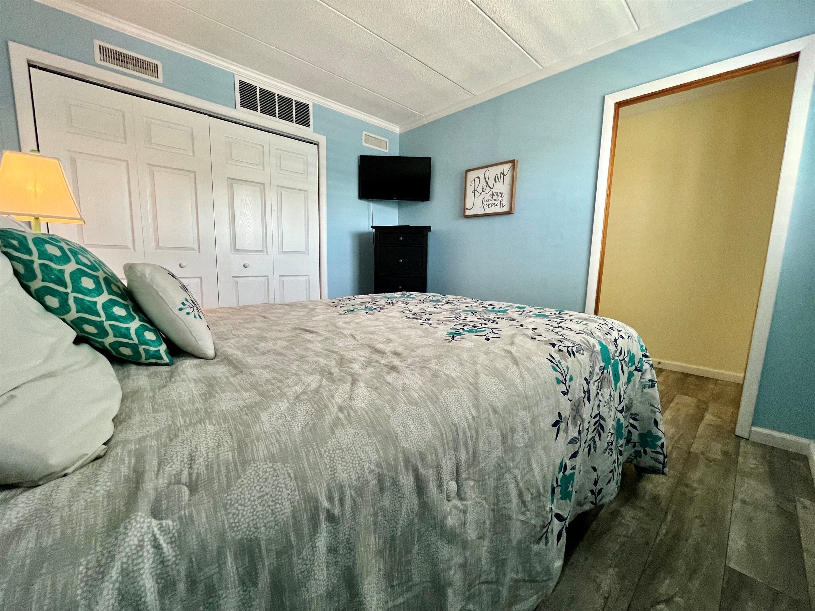 A bedroom with a bed, a TV, a door, and a wall with a picture.