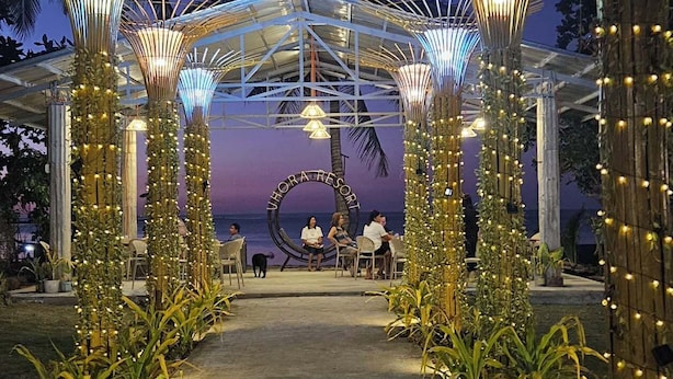 An outdoor venue with a covered seating area, palm trees, and string lights. - Vhora Resort (Cajidiocan)