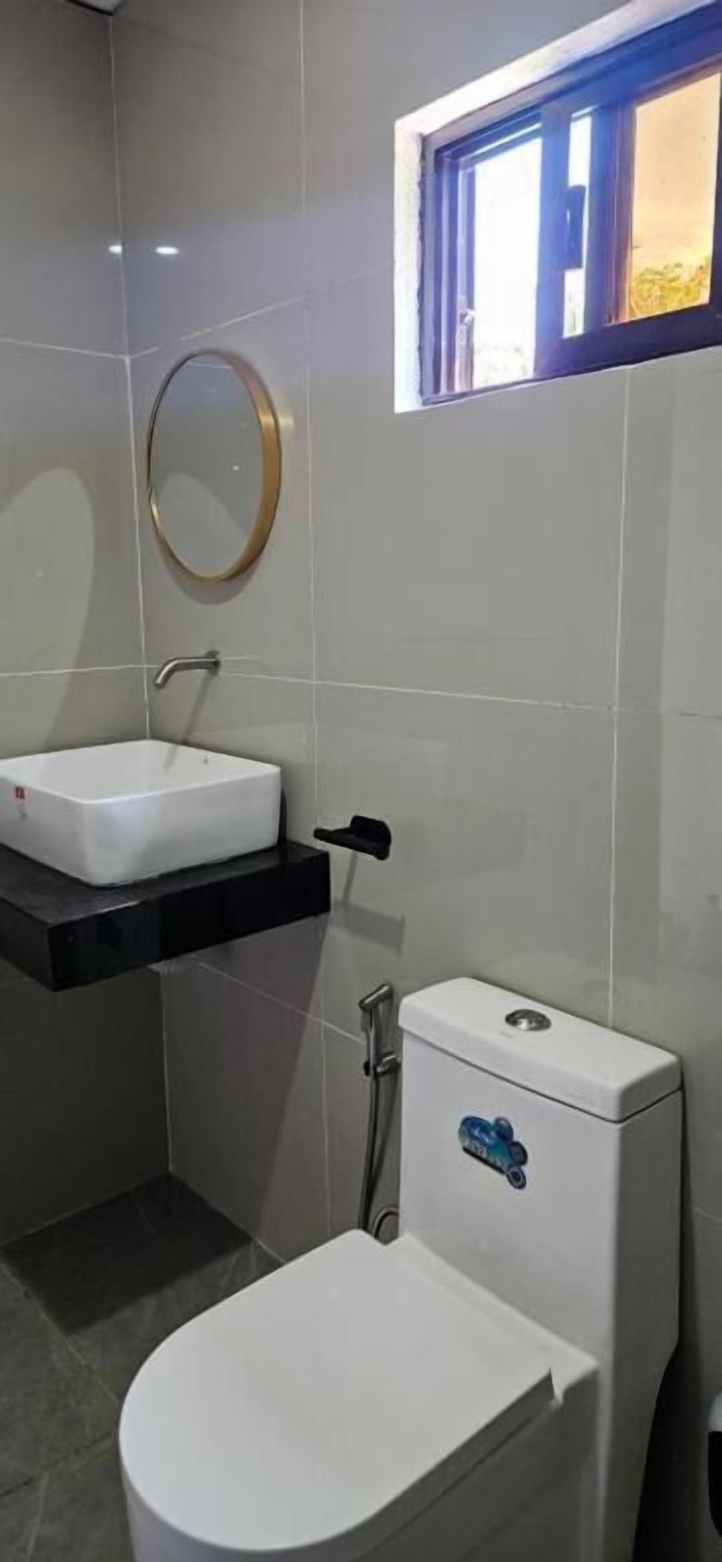 A bathroom with a white toilet, a white sink, and a window with a blue frame.